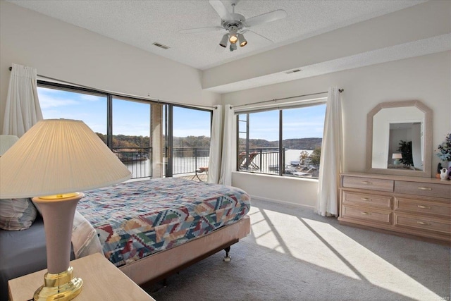 bedroom featuring a water view, a textured ceiling, light colored carpet, and ceiling fan