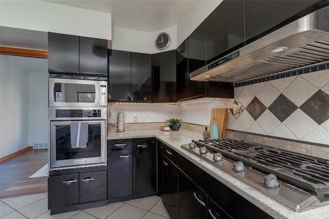 kitchen with light stone countertops, wall chimney exhaust hood, decorative backsplash, light tile patterned floors, and appliances with stainless steel finishes