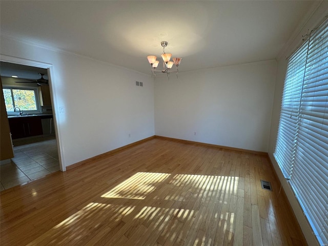 spare room featuring ornamental molding, hardwood / wood-style floors, ceiling fan with notable chandelier, and sink