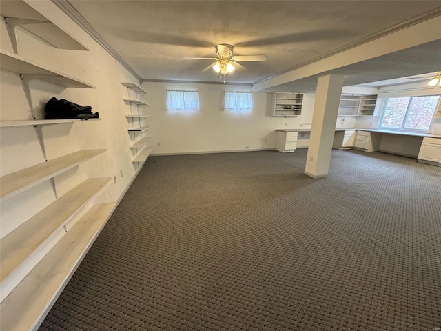 basement featuring ceiling fan, built in desk, dark carpet, and crown molding