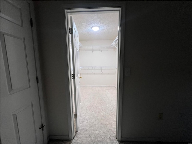 corridor with a textured ceiling and light carpet