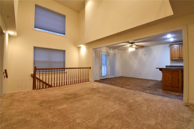 unfurnished living room with ceiling fan, dark carpet, and a high ceiling