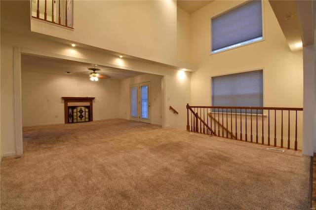 unfurnished living room with ceiling fan, carpet floors, and a high ceiling