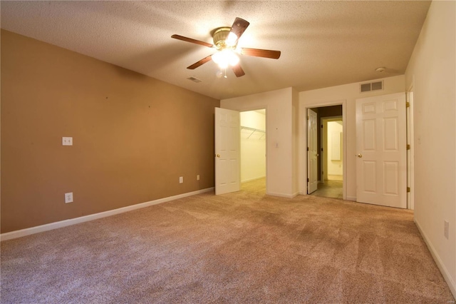 unfurnished bedroom with a walk in closet, ceiling fan, a textured ceiling, light colored carpet, and a closet