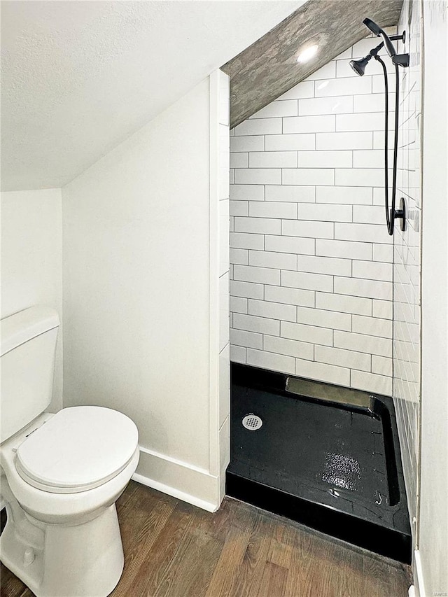 bathroom featuring a textured ceiling, vaulted ceiling, tiled shower, hardwood / wood-style floors, and toilet