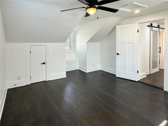 additional living space with vaulted ceiling, a barn door, ceiling fan, and dark hardwood / wood-style flooring