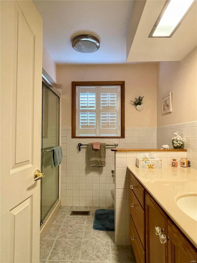 bathroom with walk in shower, vanity, tile walls, and tile patterned flooring