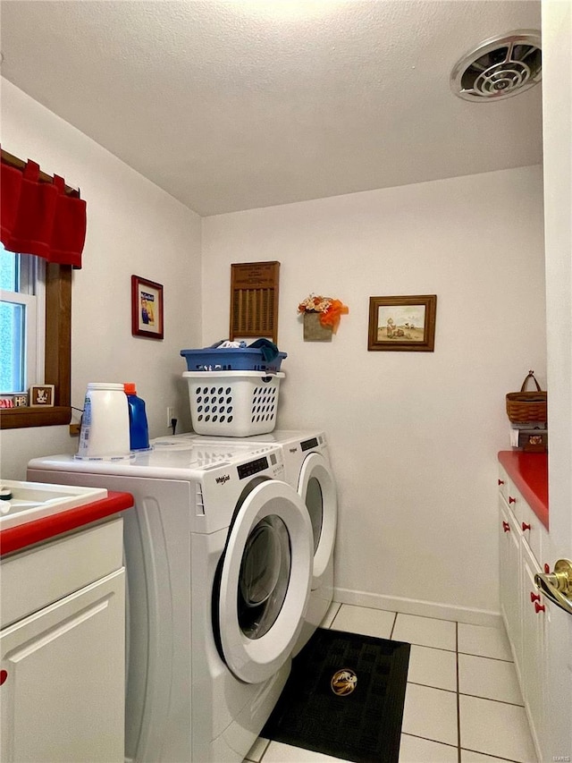 clothes washing area with cabinets, light tile patterned flooring, a textured ceiling, and washer and clothes dryer