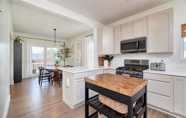 kitchen with appliances with stainless steel finishes, light wood-type flooring, decorative light fixtures, white cabinets, and a center island