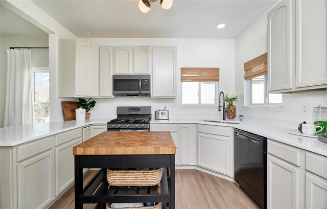 kitchen with light wood-type flooring, stainless steel appliances, sink, white cabinetry, and a kitchen island