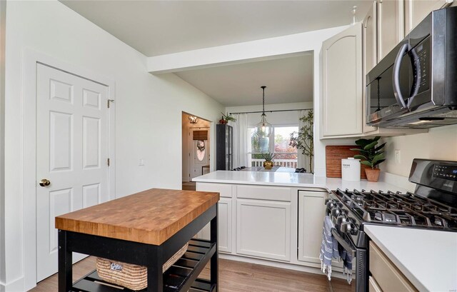 kitchen with white cabinets, decorative light fixtures, wood-type flooring, and stainless steel appliances