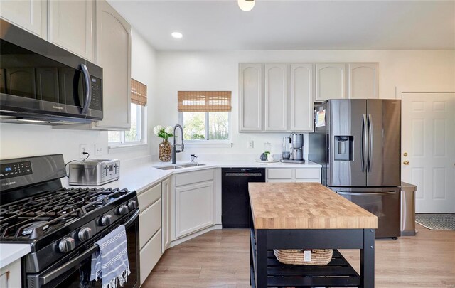 kitchen featuring black appliances, sink, butcher block countertops, light hardwood / wood-style floors, and white cabinetry