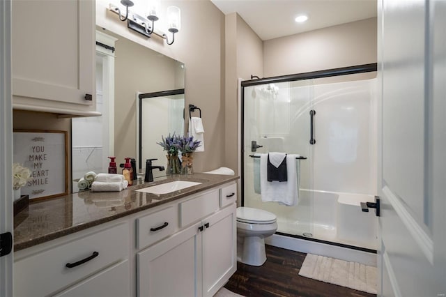 bathroom with hardwood / wood-style flooring, a shower with shower door, vanity, and toilet