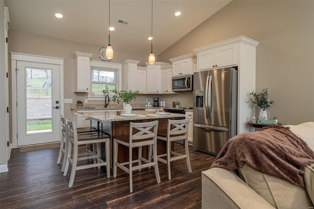 kitchen with white cabinetry, appliances with stainless steel finishes, light stone countertops, hanging light fixtures, and vaulted ceiling