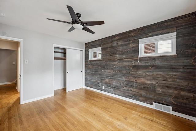 unfurnished bedroom featuring hardwood / wood-style floors, a closet, ceiling fan, and wood walls