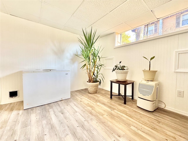 interior space featuring hardwood / wood-style flooring, a paneled ceiling, wood walls, and refrigerator