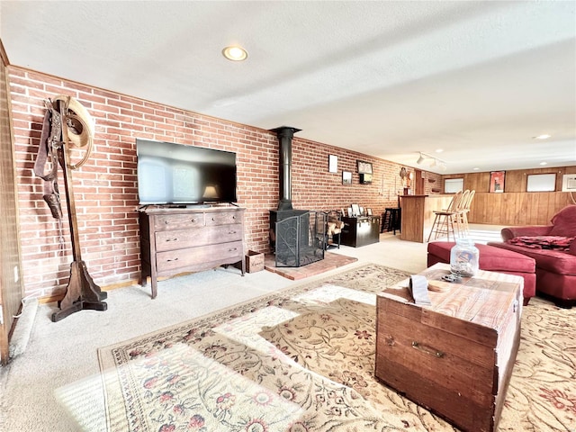 living room with a textured ceiling, light colored carpet, a wood stove, and brick wall