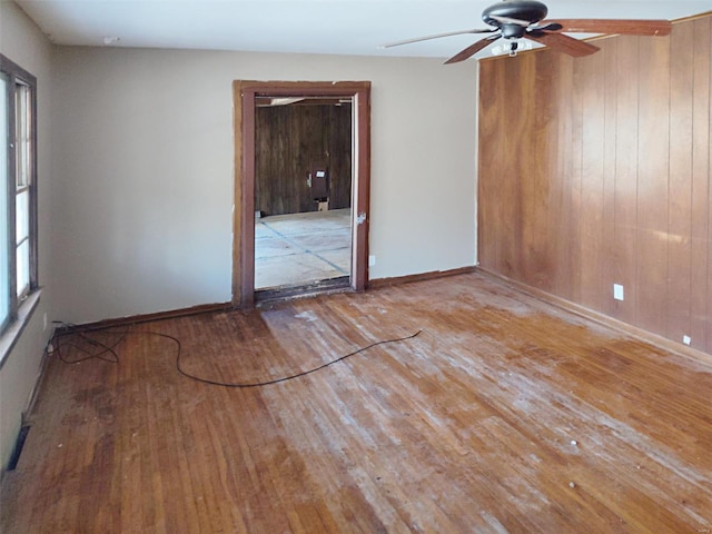 spare room with ceiling fan, wood-type flooring, and wood walls