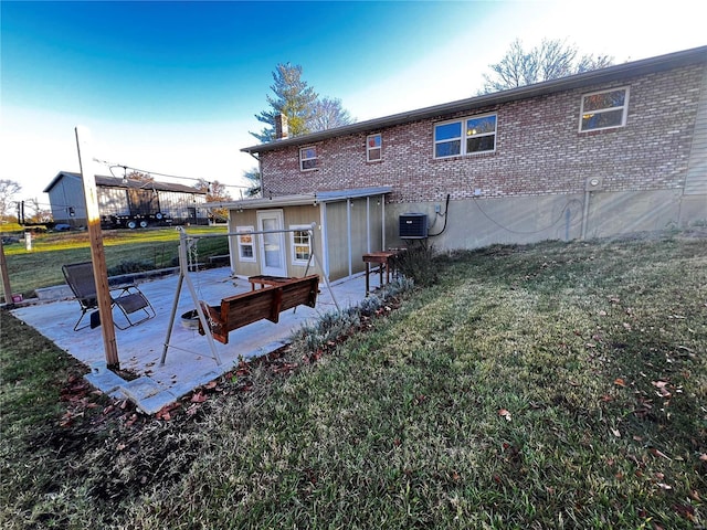 back of property featuring central AC, brick siding, a lawn, a chimney, and a patio area