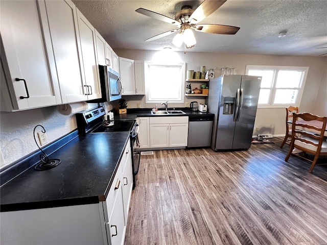 kitchen with dark countertops, light wood-style flooring, appliances with stainless steel finishes, open shelves, and a sink