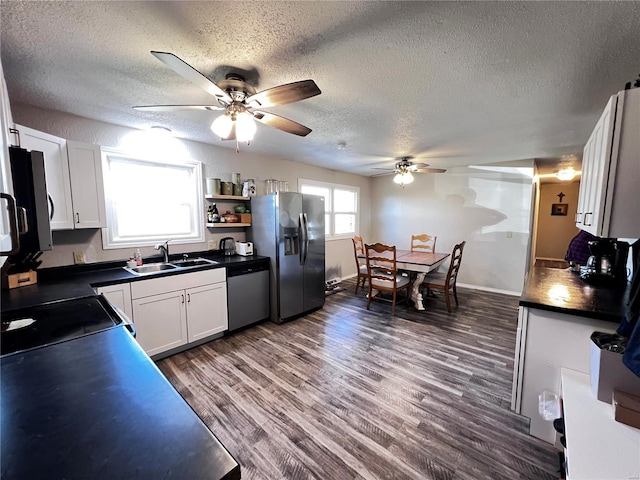 kitchen featuring white cabinets, dark countertops, dark wood-type flooring, stainless steel appliances, and a sink