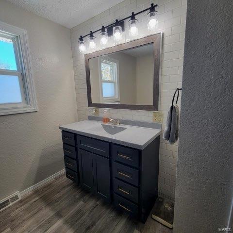 bathroom with visible vents, a textured wall, wood finished floors, a textured ceiling, and vanity