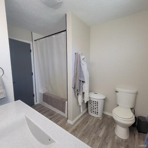 full bath featuring a textured ceiling, toilet, wood finished floors, baseboards, and a shower with curtain