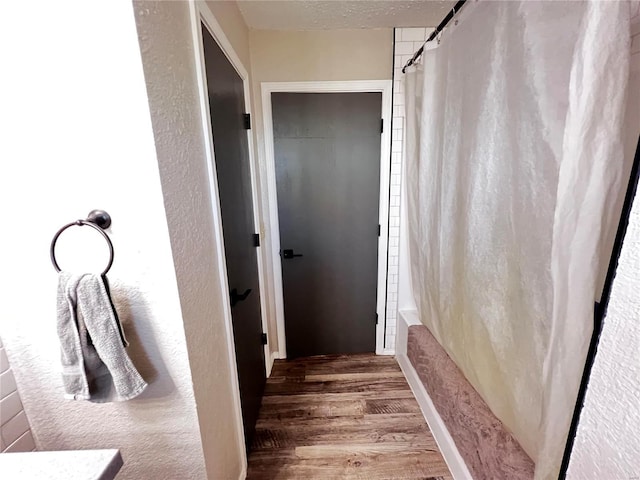 full bathroom with shower / tub combo, a textured wall, a textured ceiling, and wood finished floors