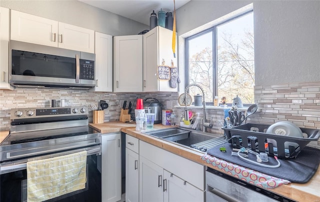 kitchen featuring stainless steel appliances, butcher block counters, sink, white cabinets, and decorative backsplash