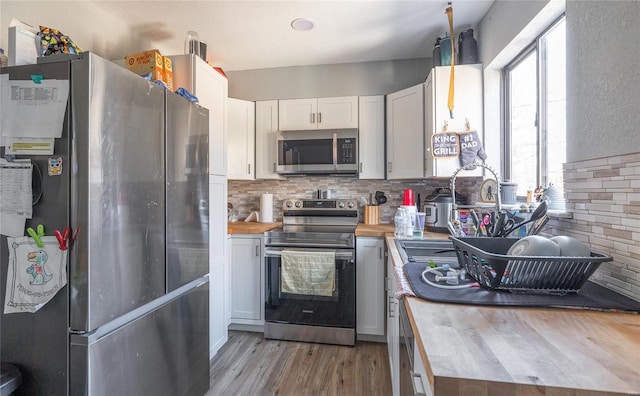 kitchen featuring stainless steel appliances, white cabinetry, backsplash, wood counters, and light hardwood / wood-style flooring