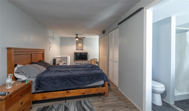 bedroom with a closet, wood-type flooring, a barn door, a textured ceiling, and ceiling fan