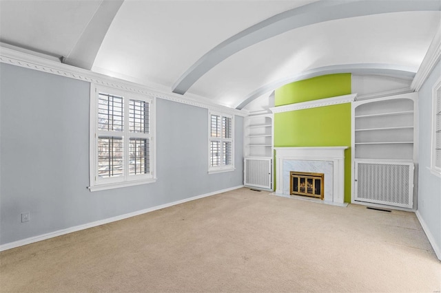 unfurnished living room featuring vaulted ceiling, light colored carpet, a fireplace, and built in shelves