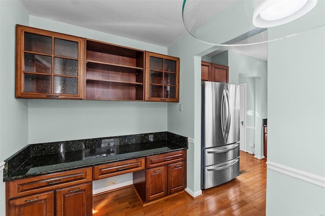 kitchen with dark stone countertops, built in desk, stainless steel fridge, and light wood-type flooring