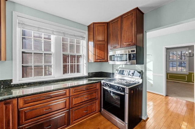 kitchen featuring plenty of natural light, stainless steel appliances, light wood-type flooring, and dark stone counters