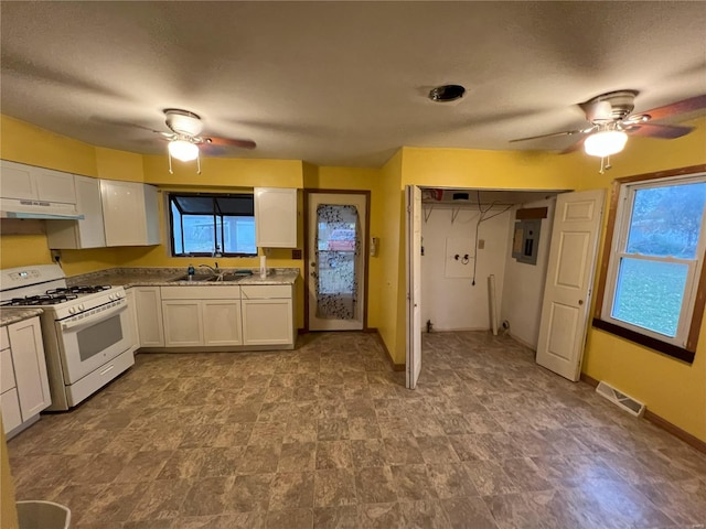 kitchen with light stone countertops, white cabinetry, sink, and gas range gas stove