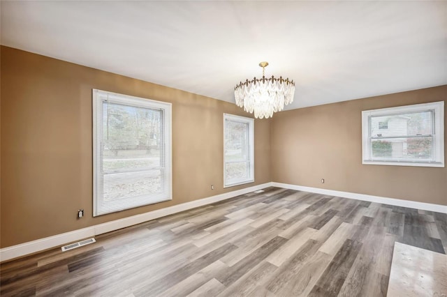 spare room with plenty of natural light, light hardwood / wood-style floors, and a chandelier