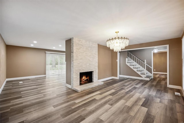 unfurnished living room featuring hardwood / wood-style flooring, a notable chandelier, and a stone fireplace