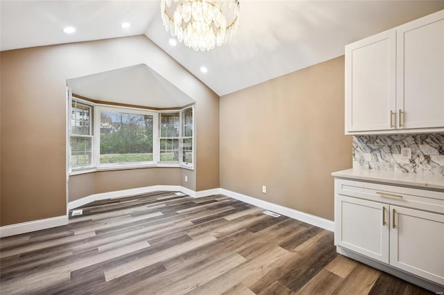 unfurnished dining area featuring hardwood / wood-style flooring, an inviting chandelier, and vaulted ceiling