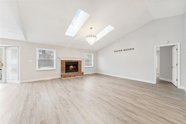 unfurnished living room with high vaulted ceiling, a brick fireplace, a skylight, a notable chandelier, and light hardwood / wood-style floors