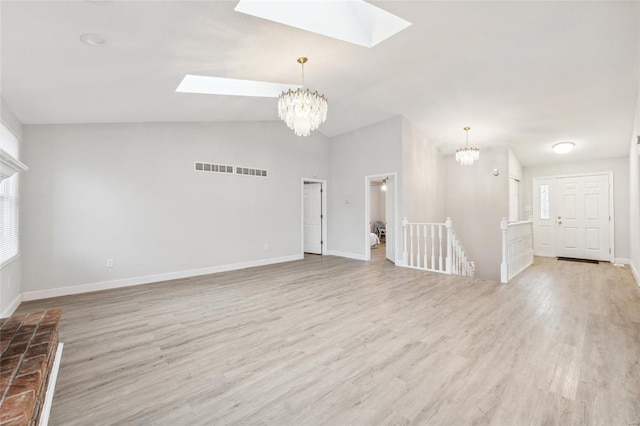 spare room with a chandelier, light wood-type flooring, and vaulted ceiling with skylight