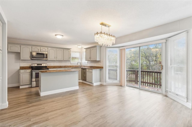 kitchen featuring appliances with stainless steel finishes, light hardwood / wood-style floors, decorative light fixtures, and gray cabinetry