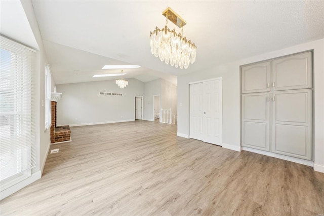 unfurnished living room with a fireplace, vaulted ceiling with skylight, light hardwood / wood-style floors, and an inviting chandelier