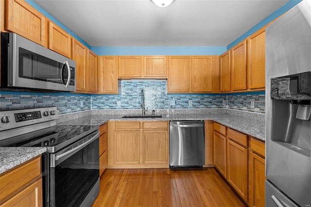 kitchen with light stone countertops, sink, light hardwood / wood-style floors, decorative backsplash, and appliances with stainless steel finishes