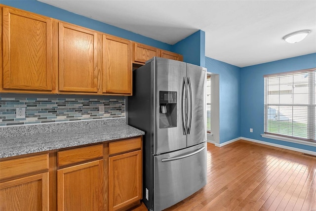 kitchen with light stone countertops, backsplash, stainless steel fridge with ice dispenser, and light hardwood / wood-style floors