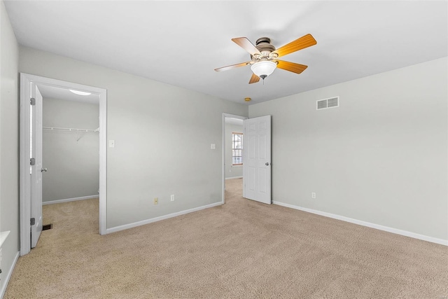 unfurnished bedroom featuring light carpet, a walk in closet, a closet, and ceiling fan