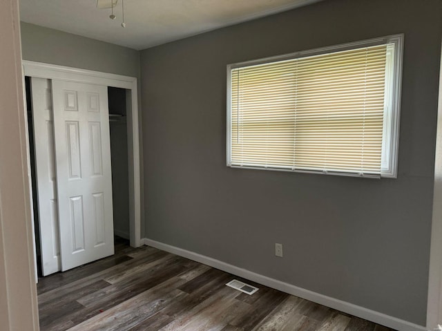 unfurnished bedroom with a closet, dark wood-type flooring, and multiple windows