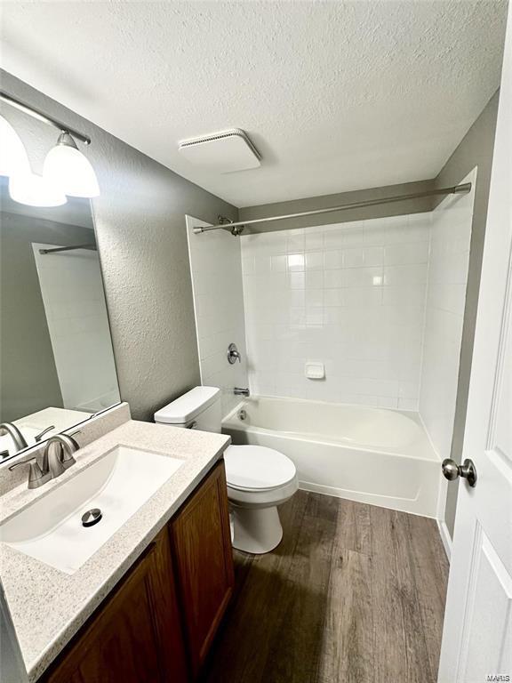 full bathroom with shower / tub combination, a textured ceiling, wood-type flooring, vanity, and toilet