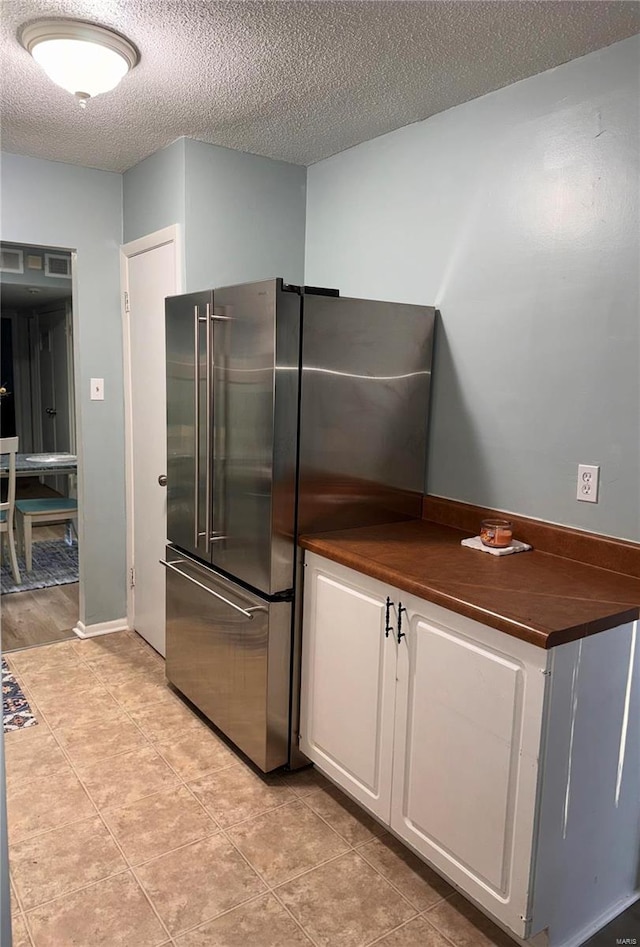 kitchen featuring high quality fridge, white cabinetry, light tile patterned flooring, and a textured ceiling