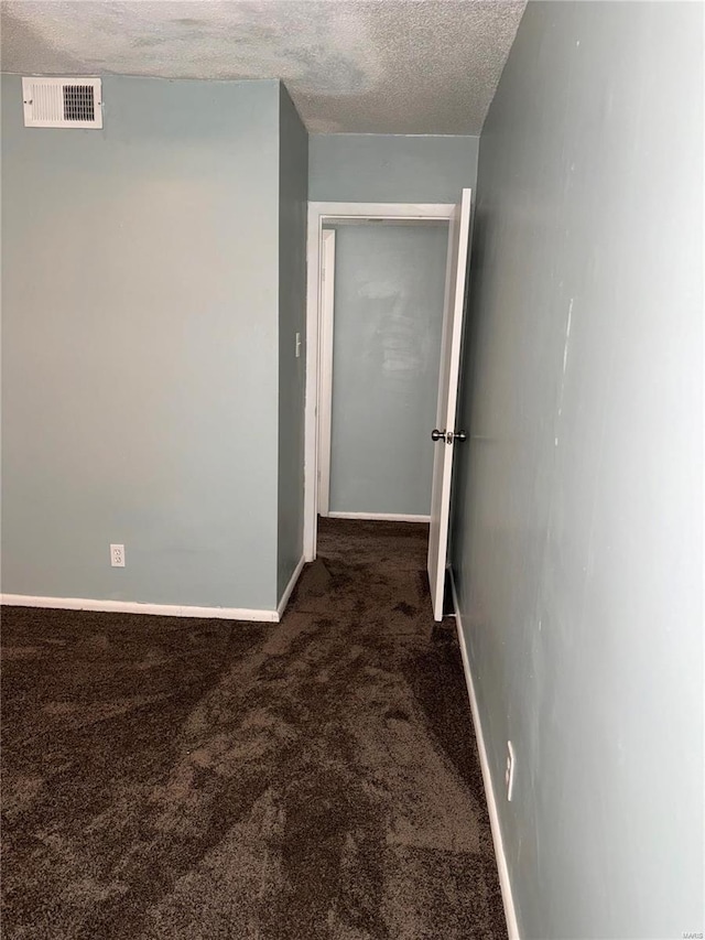 hallway featuring dark carpet and a textured ceiling