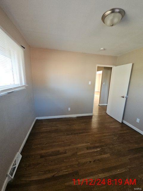 empty room featuring baseboards, visible vents, and dark wood-style flooring